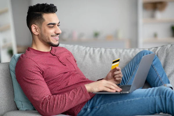 Hombre árabe alegre con tarjeta de crédito y ordenador portátil de compras en línea — Foto de Stock