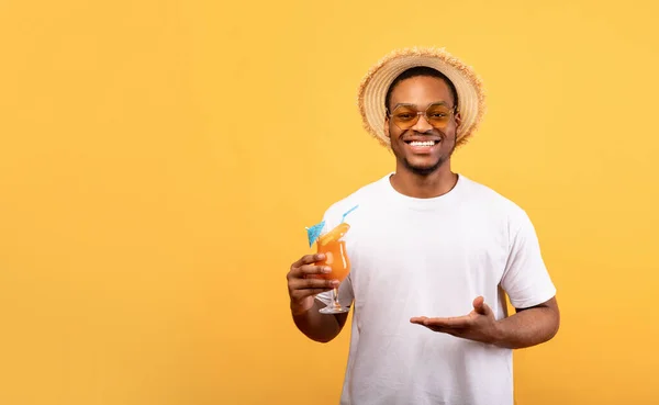 Cara preta feliz em roupa de verão oferecendo vidro de coquetel tropical no fundo amarelo, design de banner com espaço de cópia — Fotografia de Stock