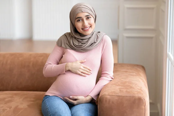 Mulher Muçulmana Grávida Em Hijab Sentado No Sofá Em Casa — Fotografia de Stock