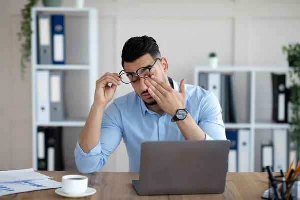 Arabischer Geschäftsmann mit müden gereizten Augen, sitzt am Schreibtisch vor dem Laptop, erschöpft von der Online-Arbeit im Büro — Stockfoto