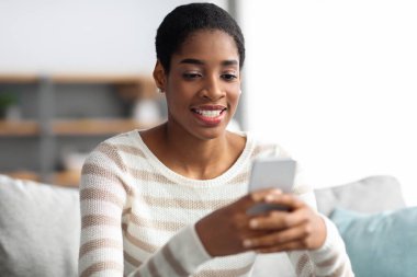 Gülümseyen Afrikalı Amerikalı Kadın Evde dinlenirken Akıllı Telefonla Mesajlaşıyor