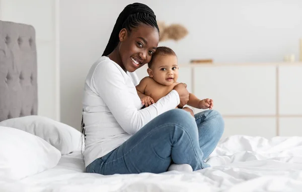 Preto mãe sentado no cama com ela bonito infantil bebê — Fotografia de Stock