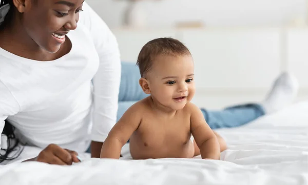 Küçük tatlı Afrikalı Amerikalı bebek annesiyle yatakta sürünüyor. — Stok fotoğraf