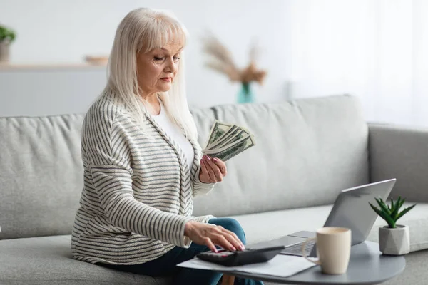 Mujer madura usando calculadora y sosteniendo dinero —  Fotos de Stock