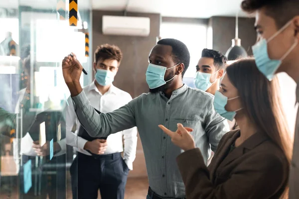 Businesspeople having meeting using sticky post-it notes on glass wall