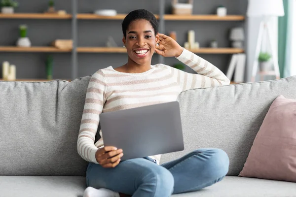 Lavoro a distanza. Ritratto di felice donna nera seduta sul divano con computer portatile — Foto Stock