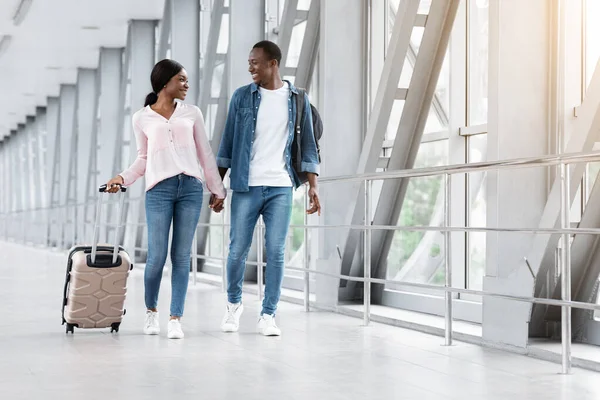 Viaje juntos. Cónyuges negros sonrientes caminando con equipaje en la terminal del aeropuerto — Foto de Stock