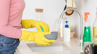 Tanınmayan bir kadın bulaşık yıkıyor, lastik eldiven giyiyor.