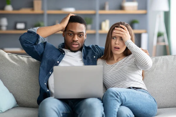 Shock Content. Frustrated interracial couple looking at laptop screen and touching heads
