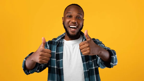Emocionado chico negro mostrando pulgares hacia arriba con ambas manos, fondo amarillo —  Fotos de Stock