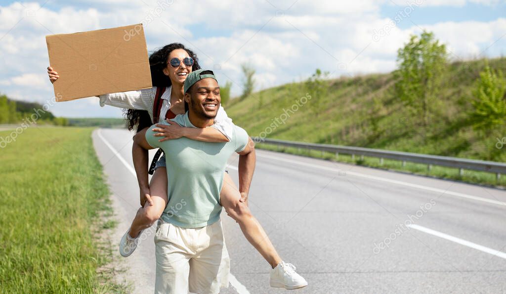 Wanderlust, autostop journey concept. Black guy and Caucasian woman hitchhiking on road with empty sign, mockup