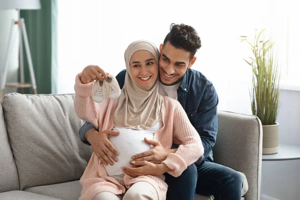 Egy boldog terhes muszlim pár portréja, akik apró babacipőket néznek. — Stock Fotó