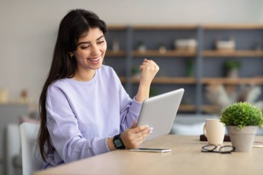 Tablet kullanan kadın yumruklarını sallayarak başarıyı kutluyor