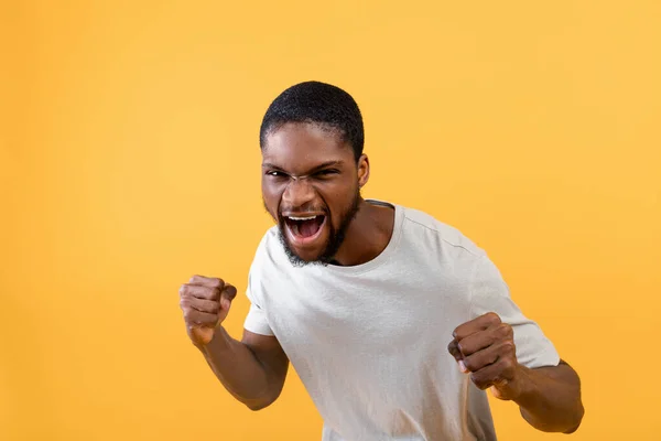 Giovane uomo nero con pugni gesto di difesa, gridando con rabbia, stringendo pugni su sfondo studio giallo — Foto Stock