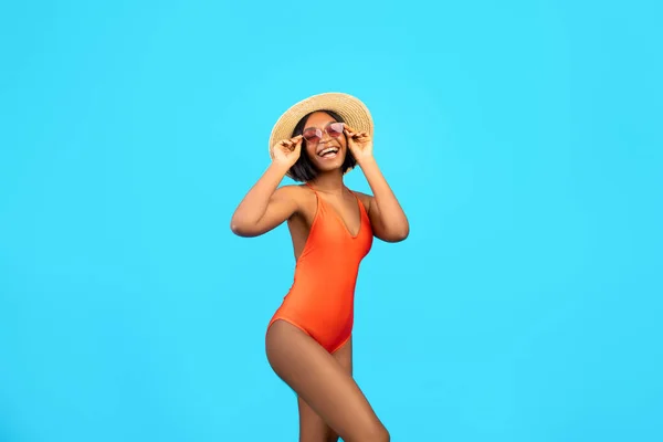 Slim sexy black lady demonstrating beach fashion, wearing stylish swimsuit, sunglasses and straw hat, smiling and posing — Stock Photo, Image