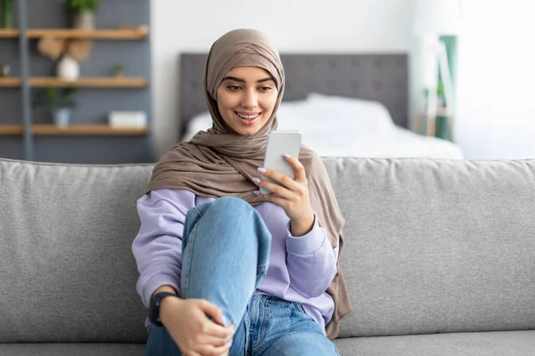 Kanepede oturan gülümseyen Müslüman kadın.