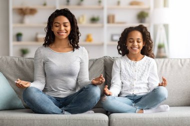 Rahat siyah anne ve kız kanepede oturmuş meditasyon yapıyorlar.