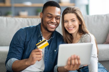 İnternetten alışveriş. Evde dijital tablet ve kredi kartı kullanan çok kültürlü bir çift.