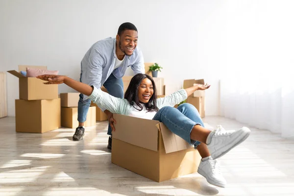 Familjen flyttar nytt ställe. Glad afrikansk man som knuffar kartonger med sin fru i. — Stockfoto