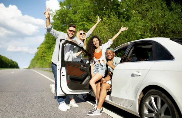 Gruppe von Millennial-Freunden posiert in der Nähe ihres Autos, winkt in die Kamera, geht auf sommerliche Roadtrip, kopiert Raum — Stockfoto