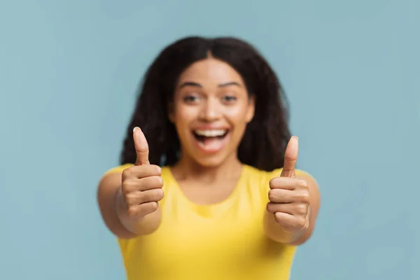 Glädjande afrikansk amerikansk kvinna visar tummen upp med båda händerna och ler mot kameran, blå bakgrund, selektivt fokus — Stockfoto
