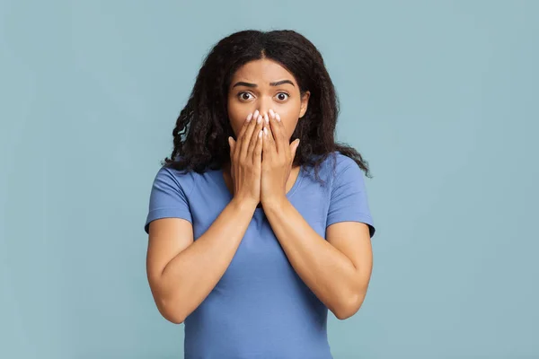 Oh nein. Schockierte und verängstigte Afroamerikanerin bedeckt ihren Mund mit Handflächen und steht vor blauem Studiohintergrund — Stockfoto