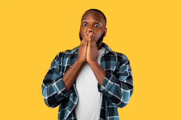 Schockierter schwarzer Millennial-Mann, der den Mund bedeckt und auf gelbem Hintergrund posiert — Stockfoto