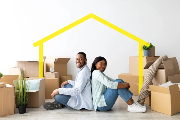 Verhuizen naar een nieuw huis. Happy Afro-Amerikaanse echtgenoten zitten op de vloer rug aan rug tussen kartonnen dozen — Stockfoto