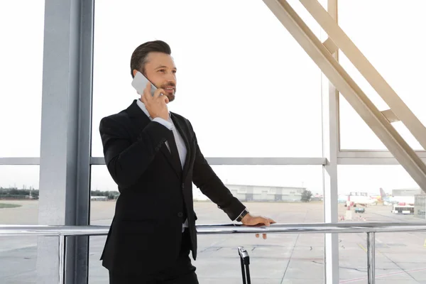 Hombre de negocios alegre de pie en el aeropuerto, hablando por teléfono —  Fotos de Stock