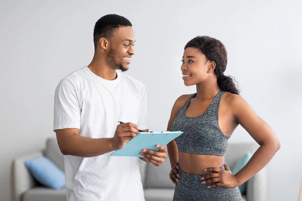 Junges schwarzes Paar diskutiert Trainingsplan und steht gemeinsam im heimischen Fitnessstudio — Stockfoto