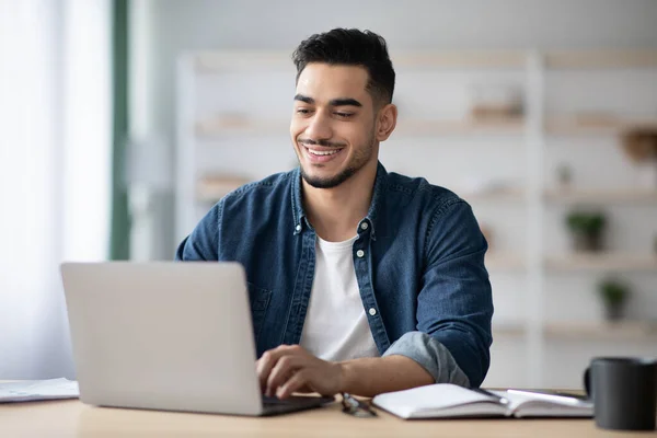 Glada arabiska killen arbetar på laptop, skriva på tangentbordet — Stockfoto