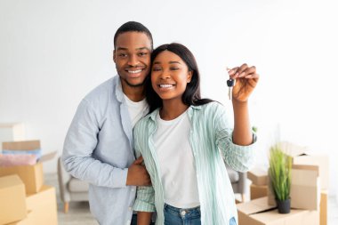 Gayrimenkul. Mutlu Afro-Amerikan çifti yeni evin anahtarını gösteriyor, karton kutuların önünde duruyorlar.