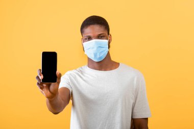 Koruyucu maskeli Afrikalı Amerikalı adam cep telefonunu kameraya gösteriyor.