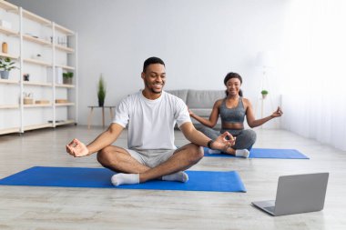 Siyahi adam kız arkadaşıyla internetten yoga yapıyor, Lotus 'un yanında poz veriyor, video dersini takip ediyor.