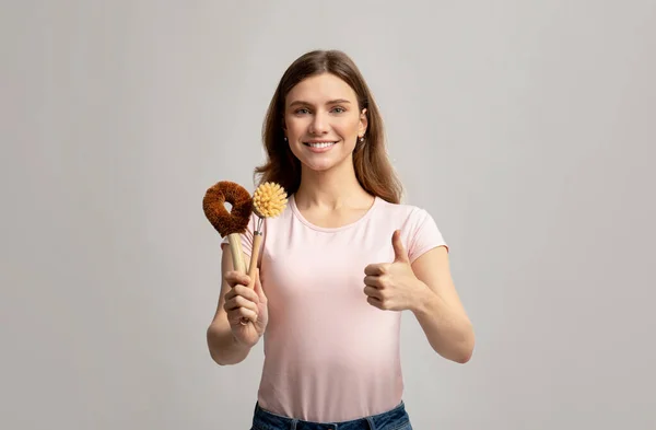 Femme gaie montrant des pinceaux naturels pour le nettoyage écologique et montrant pouce vers le haut — Photo