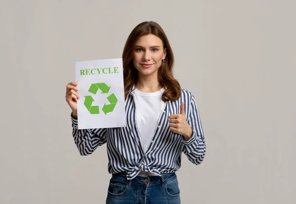 Молодая активистка-эко-активистка демонстрирует плакат со знаком "Recycle" и показывает большой палец — стоковое фото