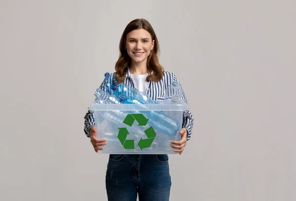 Opětovné použití odpadu. Veselá mladá žena nesoucí kontejner s plastovými lahvemi na recyklaci — Stock fotografie