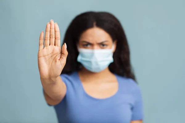 Zwarte dame die lijdt aan ziekte, het dragen van masker en voldoen aan sociale afstand, poseren over een blauwe achtergrond, studio schot. — Stockfoto