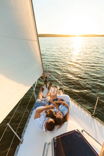 Famille relaxant allongé sur le pont de yacht regardant le coucher du soleil en plein air — Photo