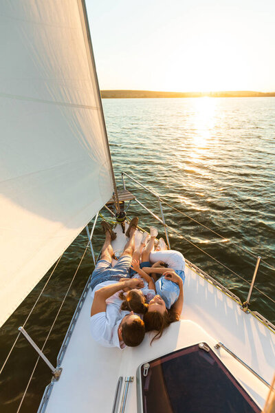 Семья отдыхает лежа на палубе яхты глядя на закат на открытом воздухе