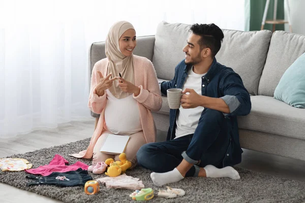 Těhotné islámské manželé Příprava dětské oblečení doma, dělat kontrolní seznam nutností — Stock fotografie