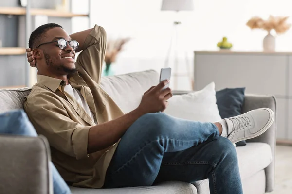 Hombre Negro Alegre Usando Teléfono Celular Usando anteojos En Casa, Vista Lateral —  Fotos de Stock