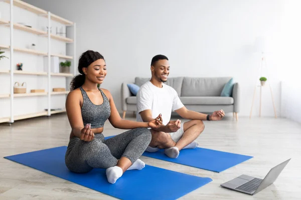 Mutlu siyah çift laptopun yanında yoga yapıyor, online video dersleri izliyor, meditasyon yapıyor ya da nefes egzersizleri yapıyor. — Stok fotoğraf