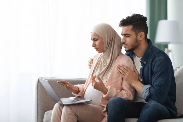 Ritratto di coppia musulmana incinta confusa guardando lo schermo del computer portatile a casa — Foto Stock