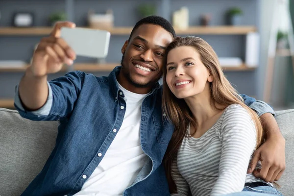 Mutlu siyah adam ve beyaz kadın evde akıllı telefondan selfie çekiyorlar. — Stok fotoğraf