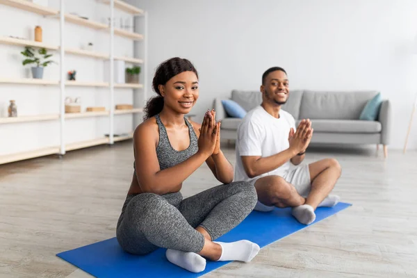 Домашня практика йоги під час ковадла. Чорна пара медитує або робить вправи, сидячи в позі лотоса вдома — стокове фото
