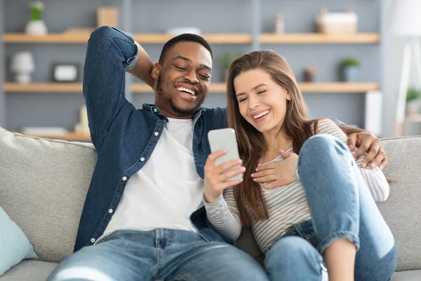 快乐的跨种族情人在家里用智能手机观看有趣的视频 — 图库照片