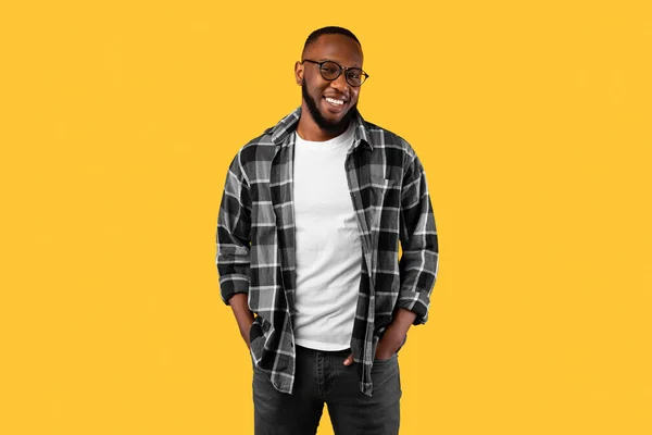 Erfolgreicher Schwarzer posiert mit Händen in Taschen, gelbem Hintergrund — Stockfoto