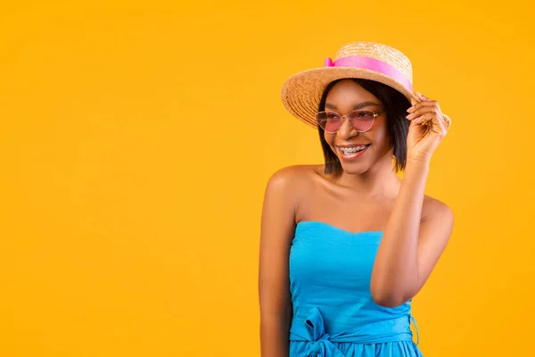 Vibrações de verão. Retrato de alegre jovem senhora negra em vestido, chapéu de palha e óculos de sol olhando para o espaço em branco — Fotografia de Stock