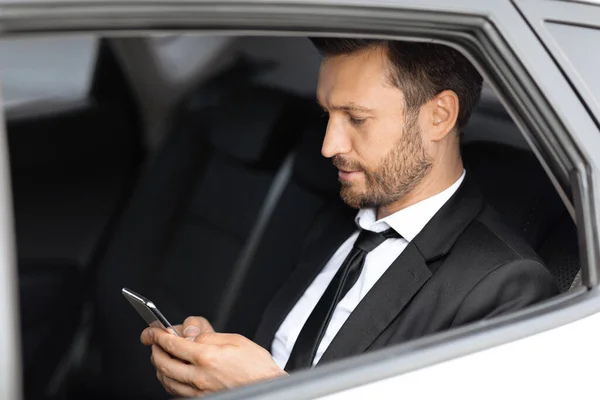 Rijke manager zit in de auto en het gebruik van de smartphone — Stockfoto